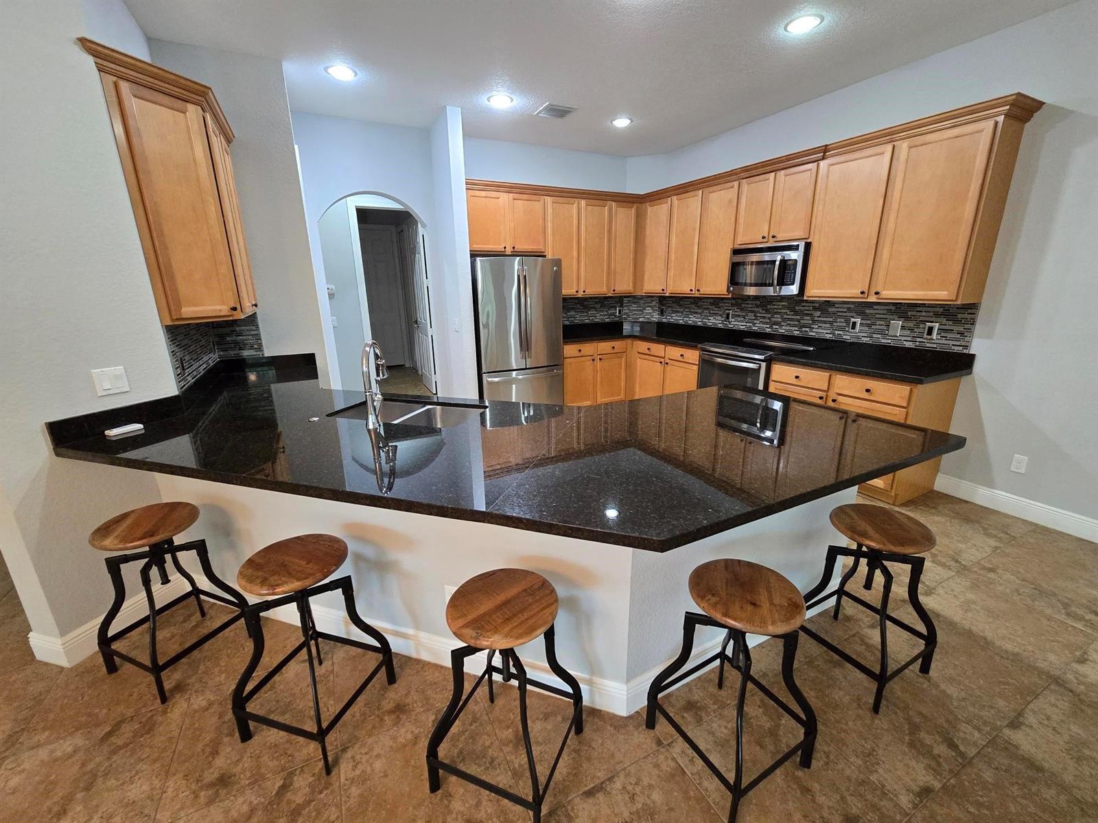 A kitchen features light wood cabinets, black granite countertops, a breakfast bar, and bar stools — 2095 NW Diamond Creek Way, Jensen Beach FL 34957, JENSEN BEACH, FL