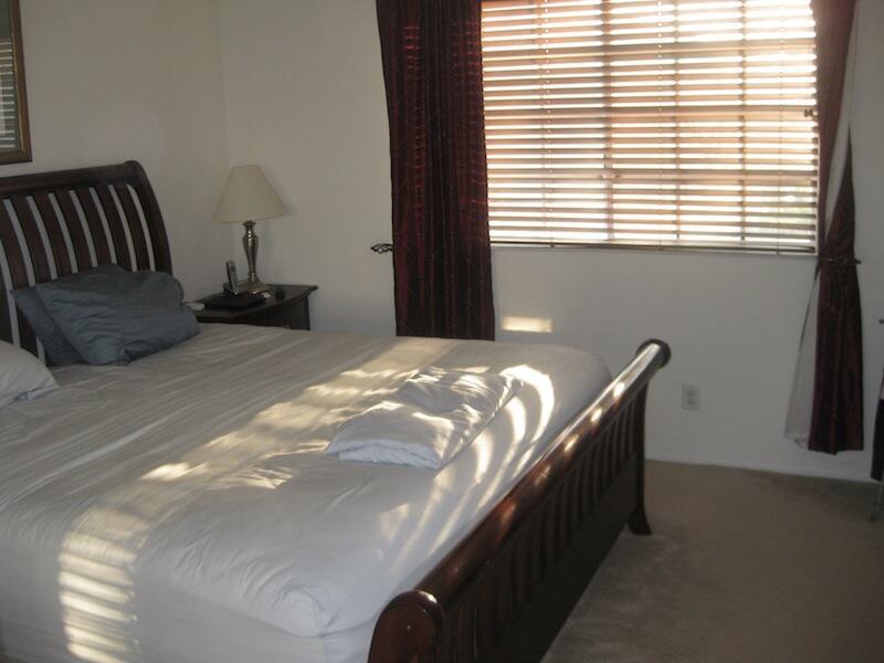 A bedroom features a wooden bed frame, a bedside lamp, and windows with horizontal blinds — 4070 NW 91st Terrace, Sunrise FL 33351, SUNRISE, FL