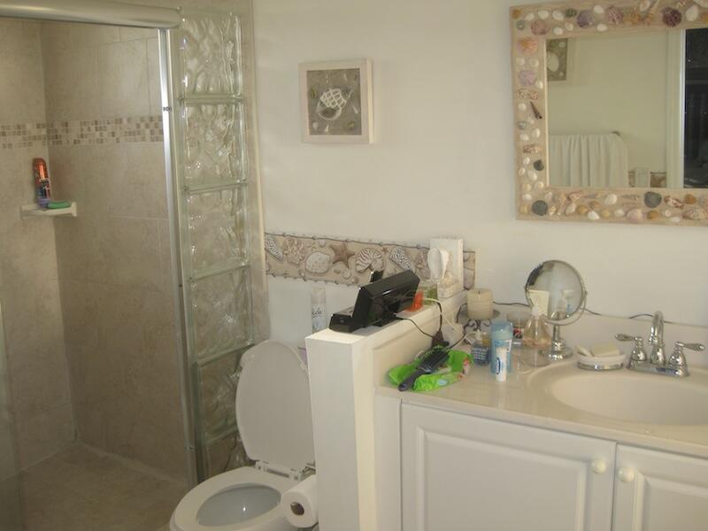 A bathroom featuring a glass block shower wall, a seashell-framed mirror, and a white vanity — 4070 NW 91st Terrace, Sunrise FL 33351, SUNRISE, FL