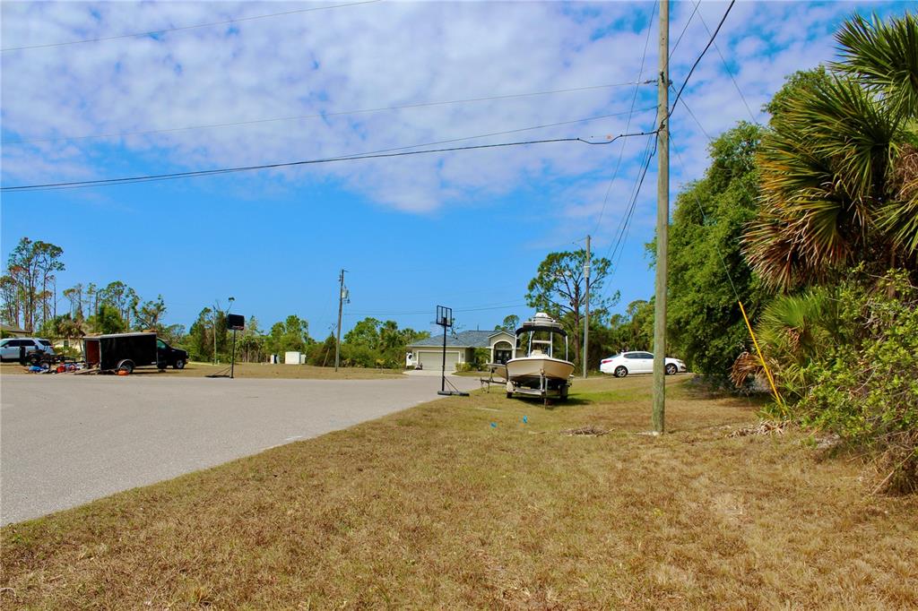 A boat on a trailer sits on a grassy lot near a paved road — 118 CABLE DRIVE, ROTONDA WEST, FL