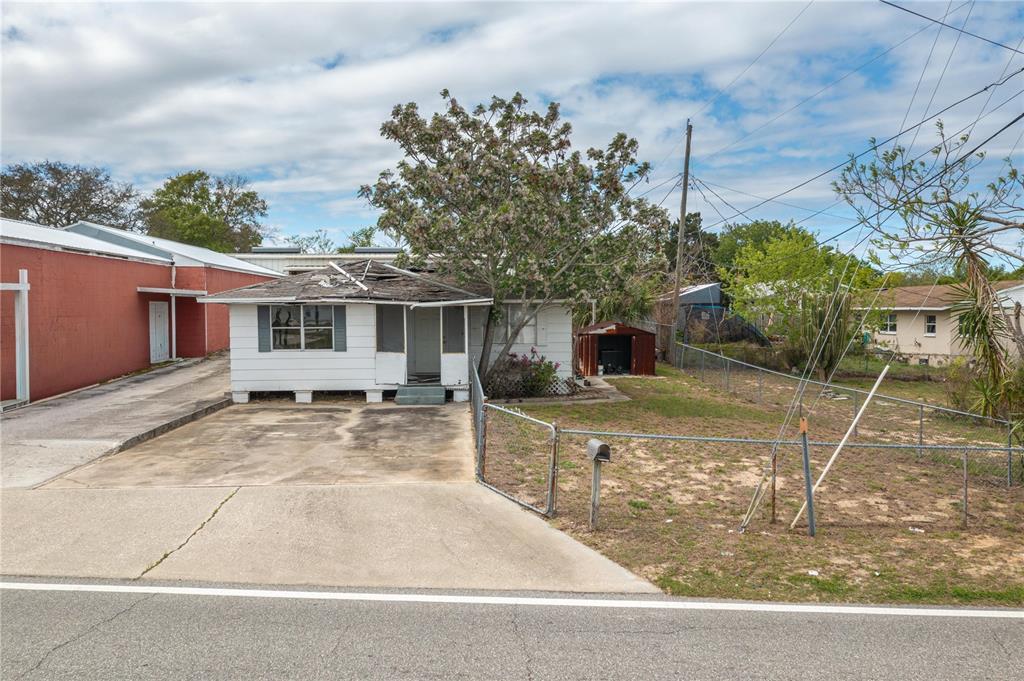 A white single-story house with a damaged roof sits behind a concrete driveway and fence — 19 EVERGREEN DRIVE, LAKE WALES, FL