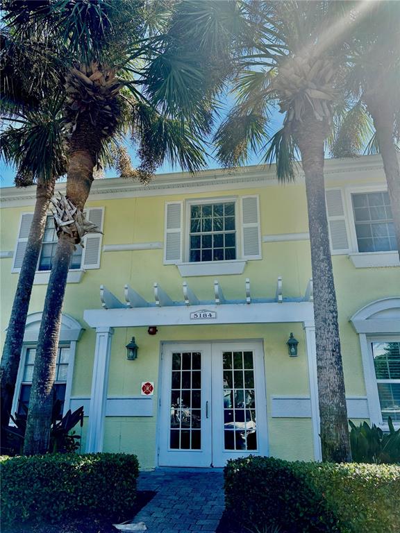 A two-story yellow building with palm trees, a pergola, and a double glass door entrance — 5184 BEACH DRIVE SE UNIT D, ST PETERSBURG, FL