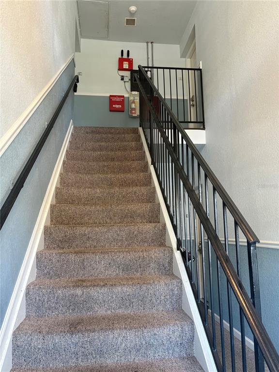 A carpeted staircase leads up to a landing with a fire alarm control panel — 5184 BEACH DRIVE SE UNIT D, ST PETERSBURG, FL
