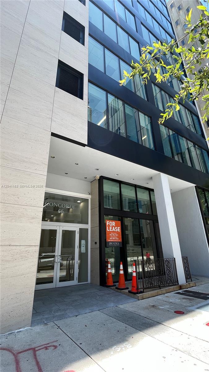 The exterior of a modern building features a glass facade, stone cladding, and a lease sign — 66 W Flagler St # 320, Miami FL 33130, MIAMI, FL