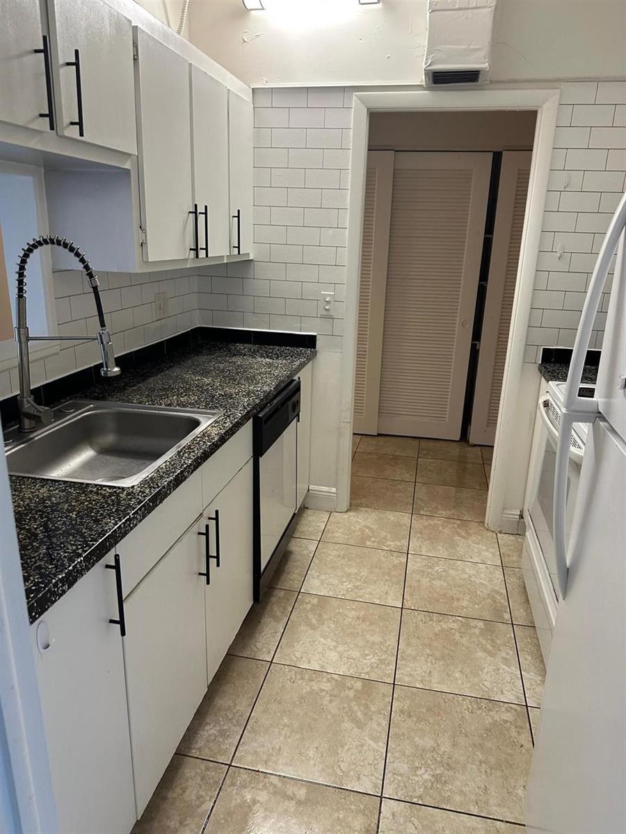A galley kitchen features white cabinets, dark granite countertops, subway tile backsplash, and tile flooring — 400 N Riverside Drive # 102, Pompano Beach FL 33062, POMPANO BEACH, FL