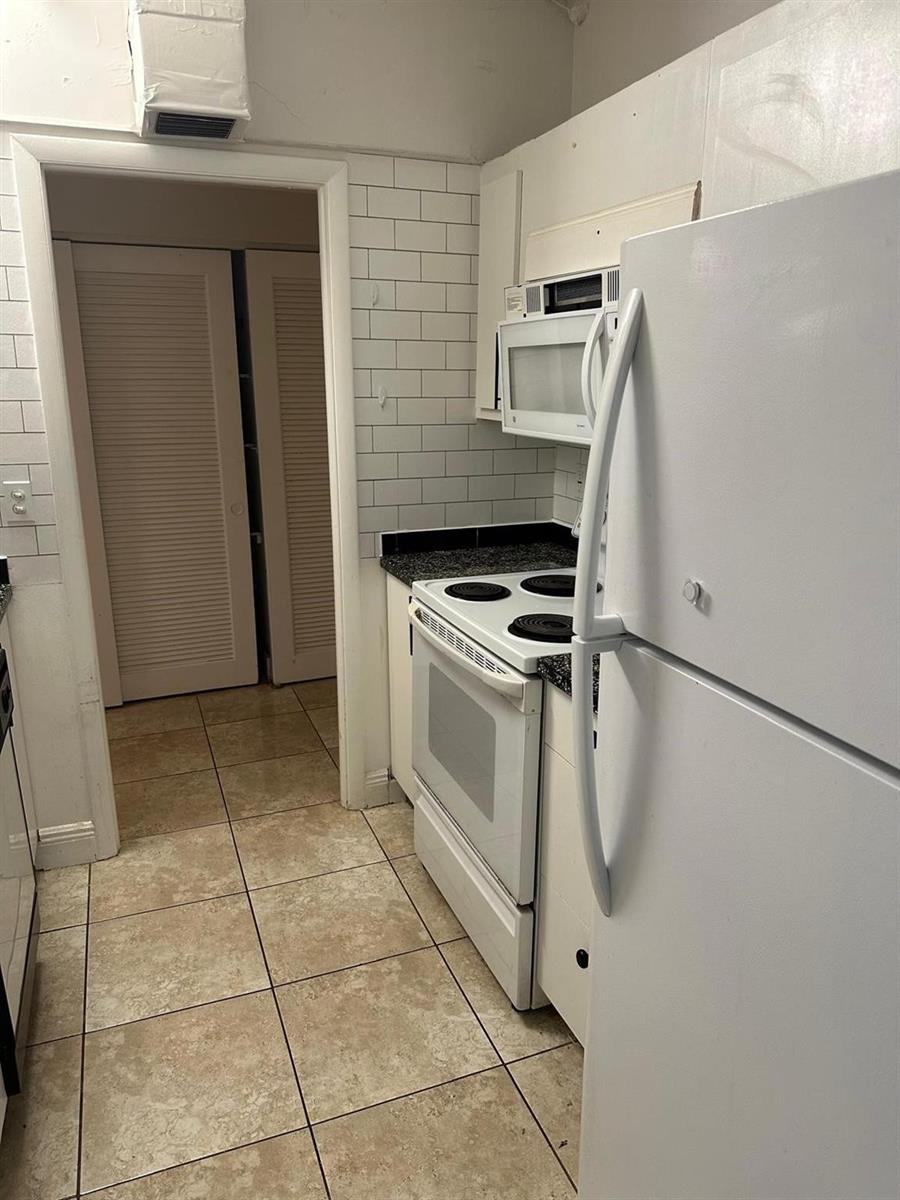 A kitchen features white appliances, subway tile backsplash, dark countertops, and light-colored floor tiles — 400 N Riverside Drive # 102, Pompano Beach FL 33062, POMPANO BEACH, FL