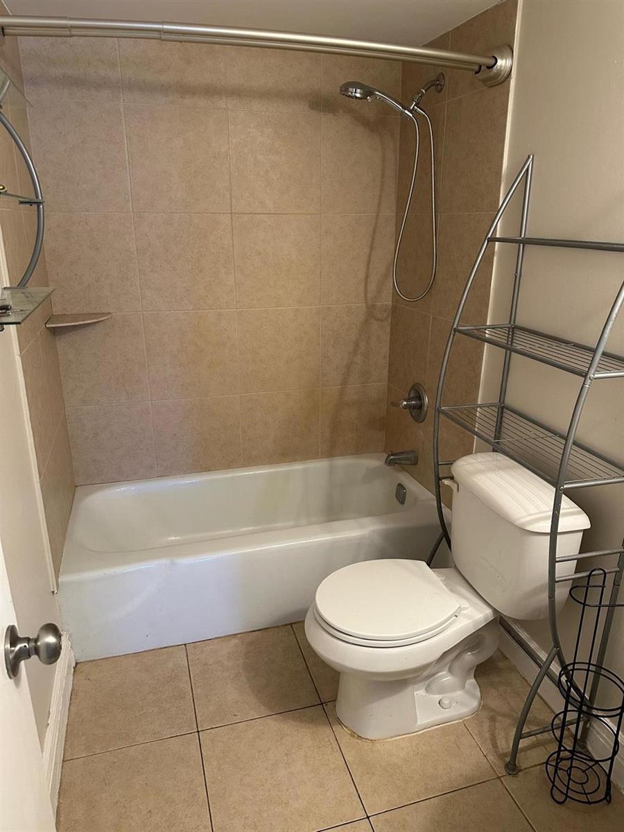 A bathroom features a tiled tub-shower combination, a white toilet, and a metal storage rack — 400 N Riverside Drive # 102, Pompano Beach FL 33062, POMPANO BEACH, FL