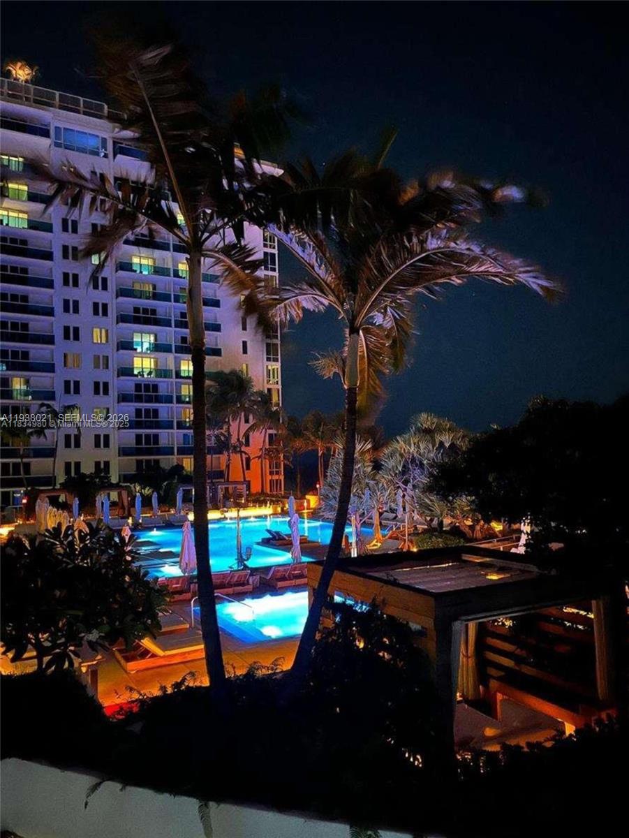 An illuminated swimming pool area at night with palm trees and a tall apartment building — 2301 Collins Ave # 423, Miami Beach FL 33139, MIAMI BEACH, FL