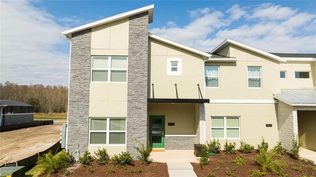 A two-story townhouse exterior features tan stucco walls, stone veneer accents, and a green door — 4355 SCENE LANE, KISSIMMEE, FL