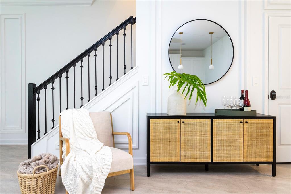 A modern entryway features a staircase, a cane-front sideboard, a round mirror, and an armchair — 4355 SCENE LANE, KISSIMMEE, FL