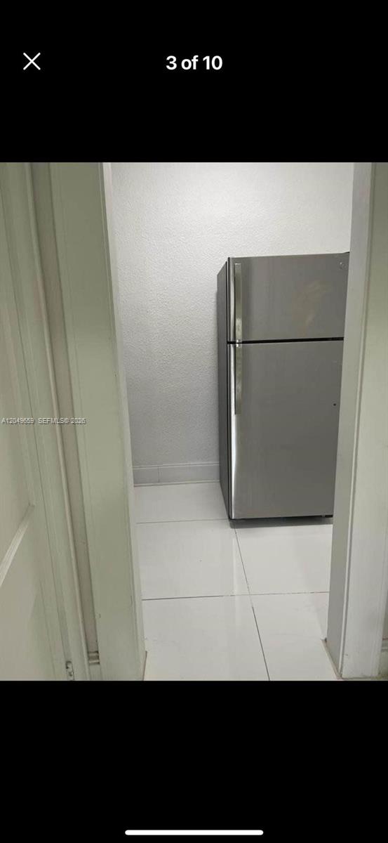 A stainless steel refrigerator sits in a small, tiled room with white walls — 126 Mendoza Ave # 1, Coral Gables FL 33134, CORAL GABLES, FL