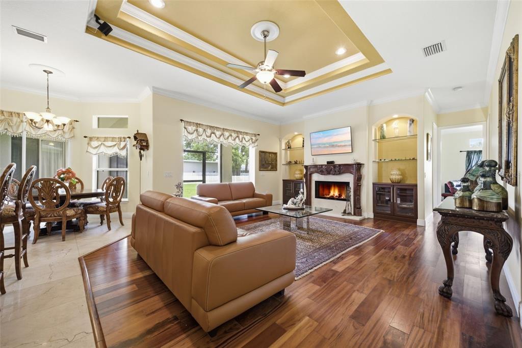 A living room with a tray ceiling, fireplace, and hardwood floors adjacent to a dining area — 17127 BROWN ROAD, ODESSA, FL