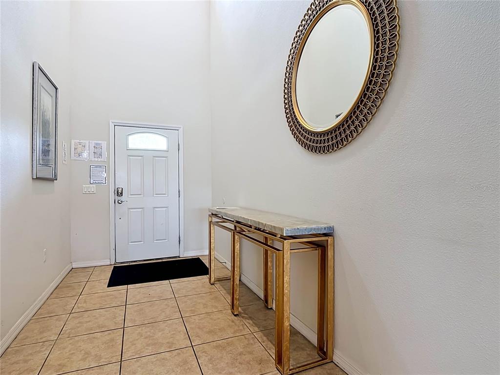An entryway features a white door, tiled floor, gold console table, and a round mirror — 1829 GOBI DRIVE, KISSIMMEE, FL