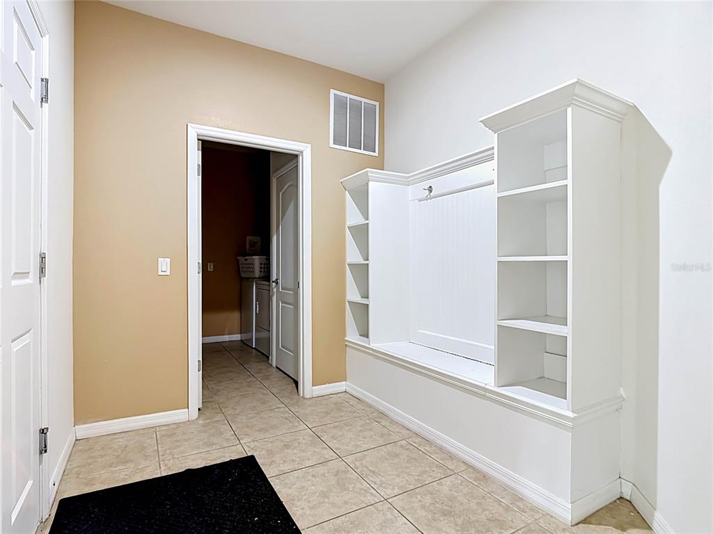 A mudroom features a white built-in storage unit, tan walls, and light-colored tile flooring — 1829 GOBI DRIVE, KISSIMMEE, FL