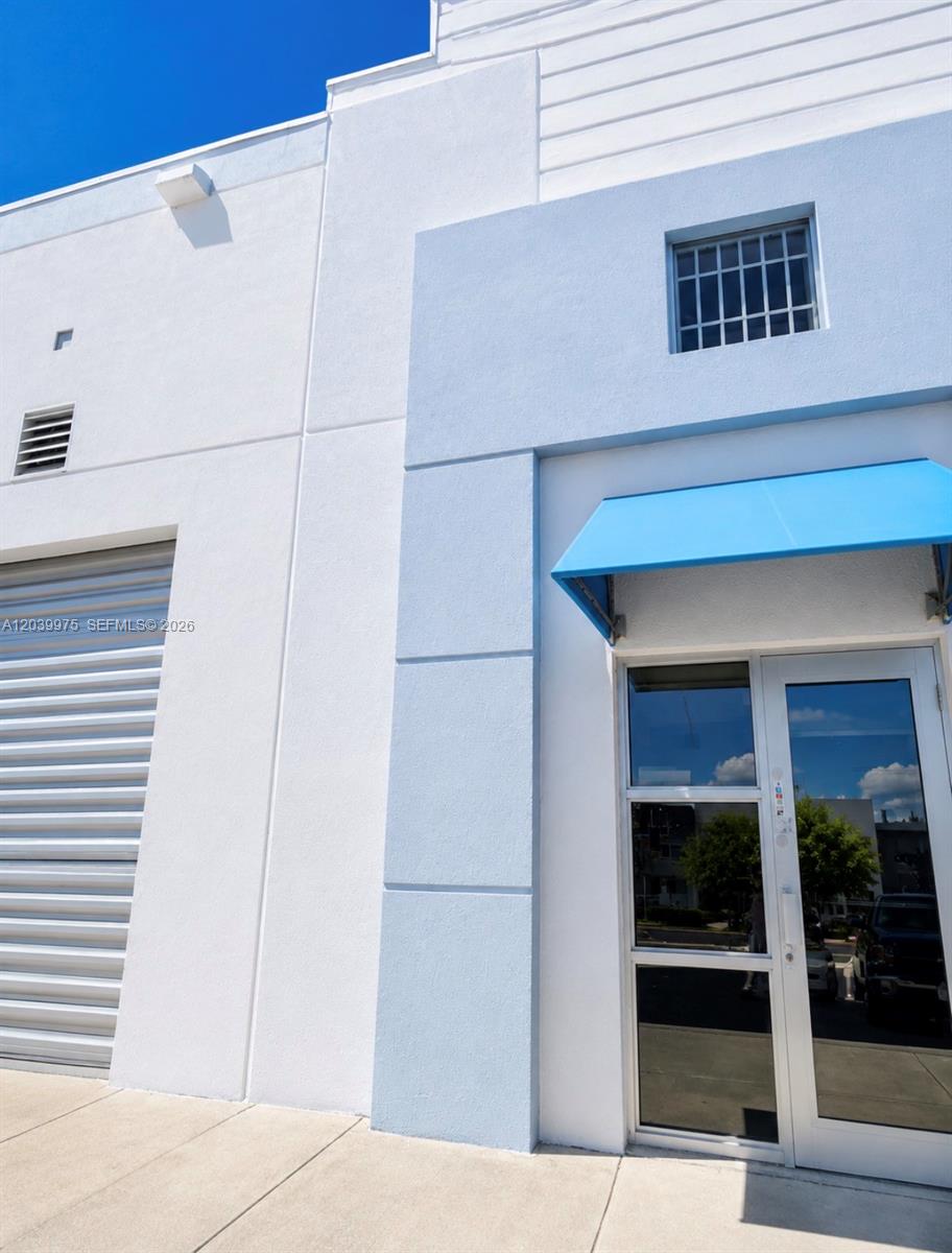 This exterior view shows a white building with a roll-up door and a glass door — MIAMI, FL