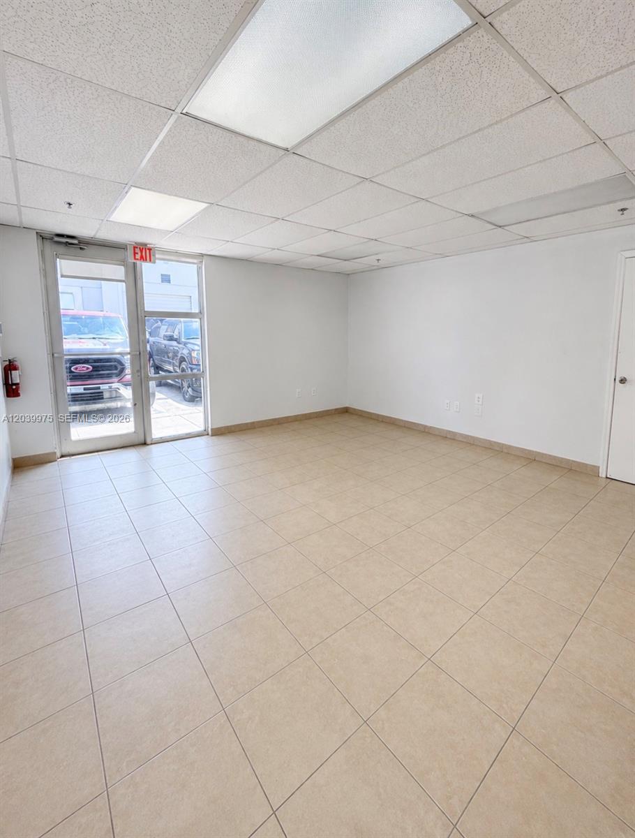 An empty office space features beige tile flooring, white walls, and a drop ceiling — MIAMI, FL