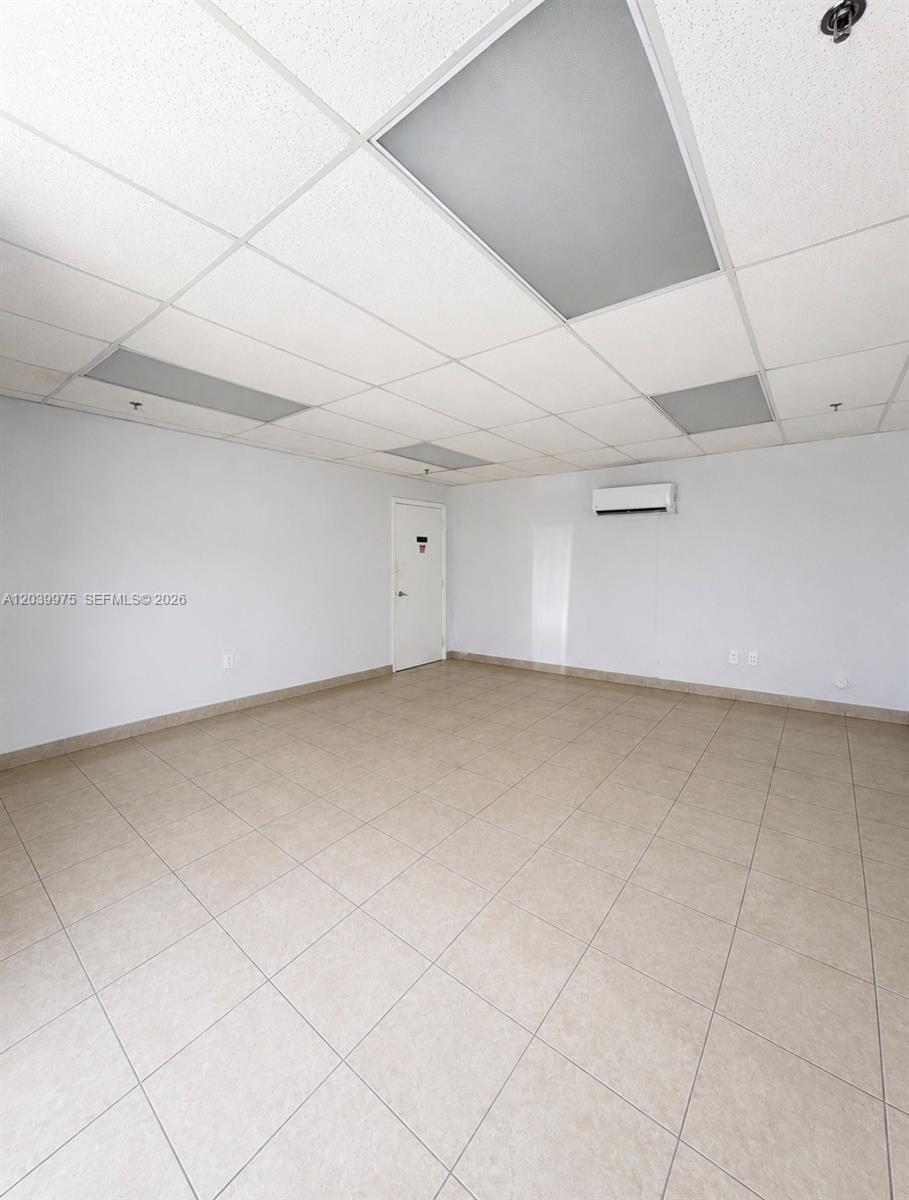 An empty room features light-colored floor tiles, white walls, a drop ceiling, and a door — MIAMI, FL