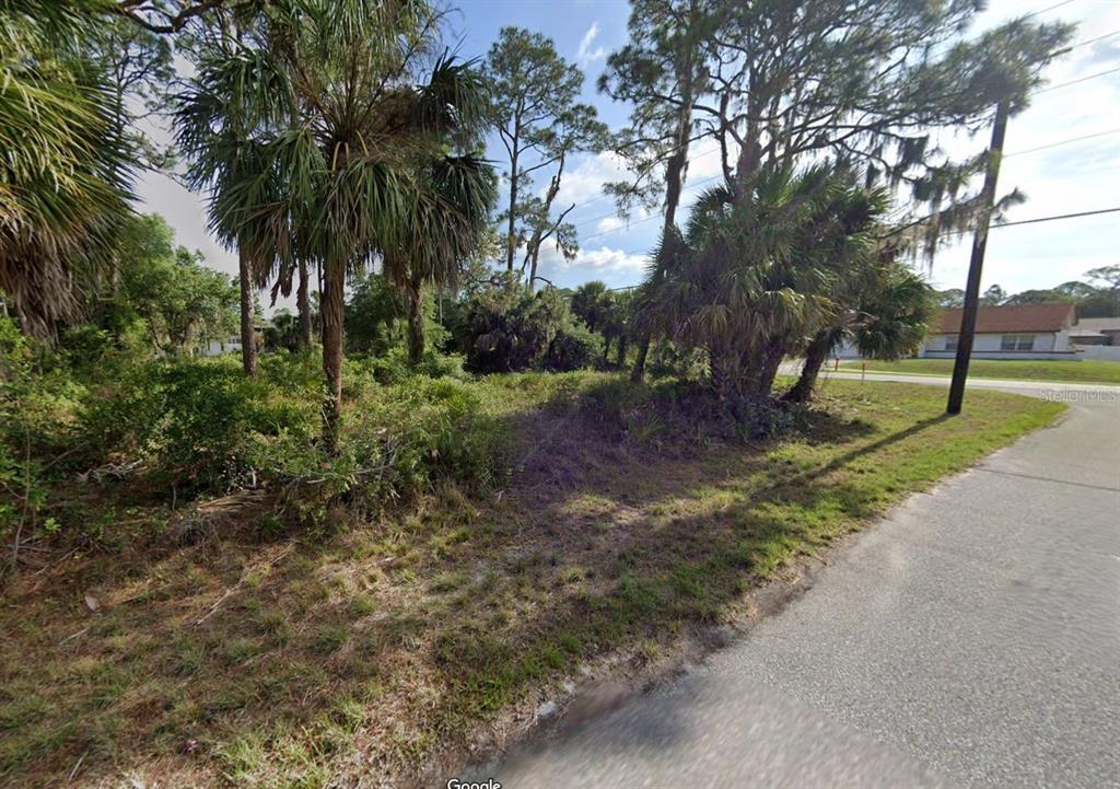 A vacant, wooded lot with palm trees and brush sits along a paved residential street — 17526 YORK AVENUE, PORT CHARLOTTE, FL