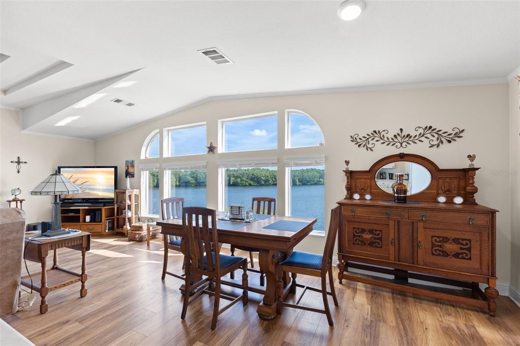 A dining room with wood floors, a wooden table, and large windows overlooking a lake — 7013 MOUNT PINEY ROAD NE UNIT 724, ST PETERSBURG, FL