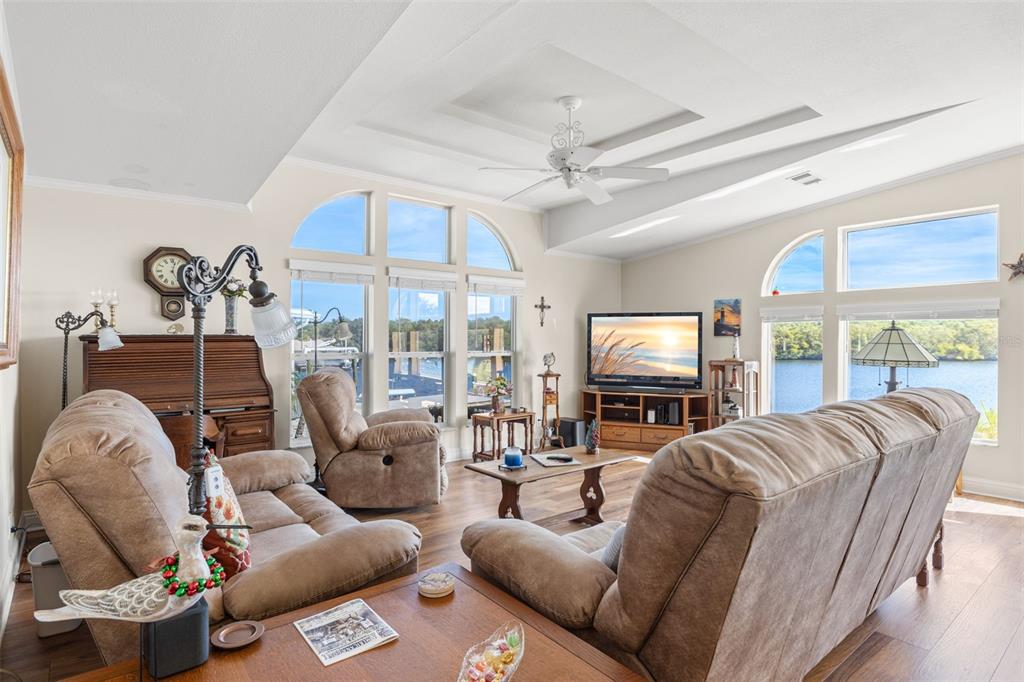 A living room features brown furniture, a ceiling fan, and large windows overlooking a waterway — 7013 MOUNT PINEY ROAD NE UNIT 724, ST PETERSBURG, FL