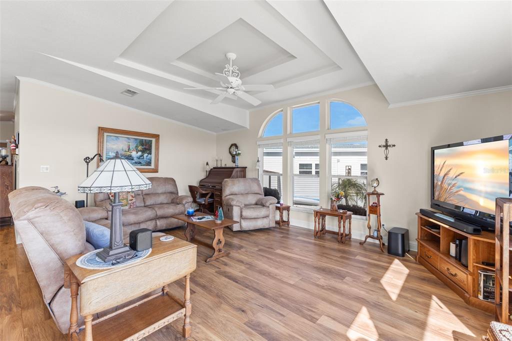 A living room with wood-look flooring, a tray ceiling, and large arched windows — 7013 MOUNT PINEY ROAD NE UNIT 724, ST PETERSBURG, FL