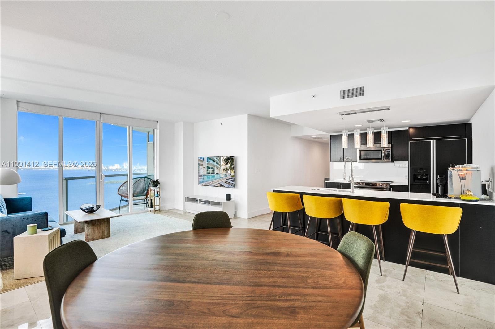 A modern open-concept living and dining area features a kitchen with yellow bar stools — 665 NE 25th St # 2105, Miami FL 33137, MIAMI, FL