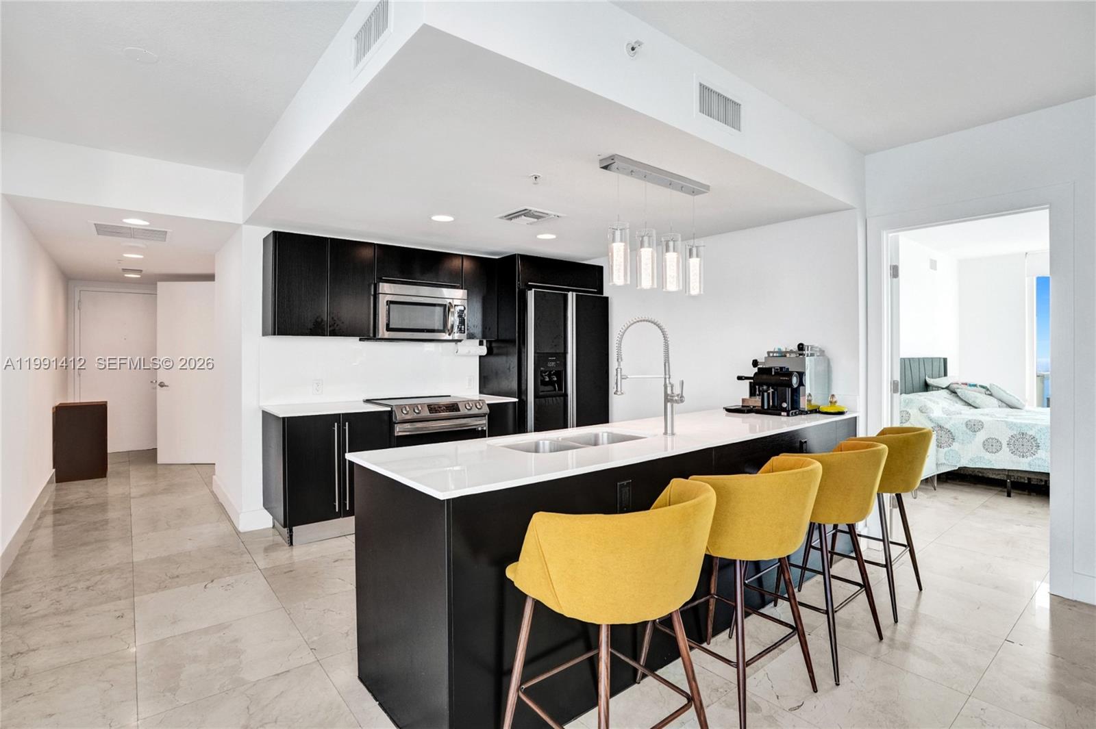 A modern kitchen features black cabinetry, a white island with yellow barstools, and tile flooring — 665 NE 25th St # 2105, Miami FL 33137, MIAMI, FL