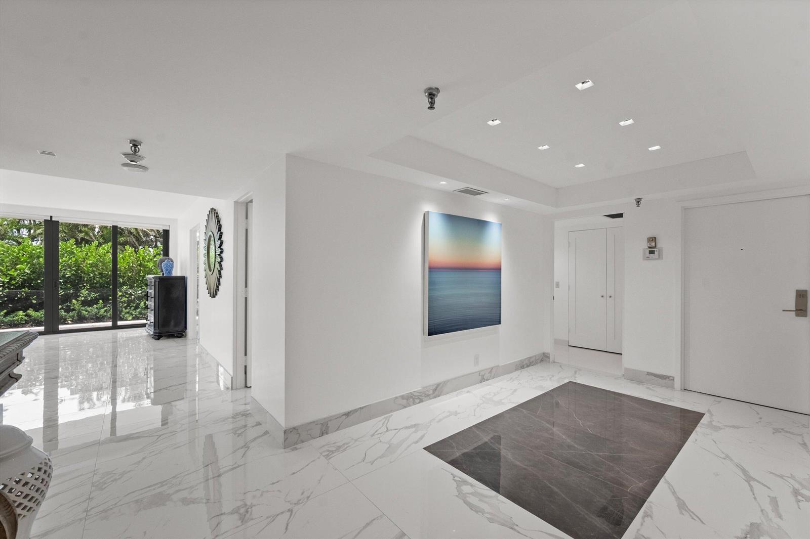 A bright, modern entryway features white marble floors, a dark stone inlay, and wall art — 2580 S Ocean Boulevard, Palm Beach FL 33480, PALM BEACH, FL