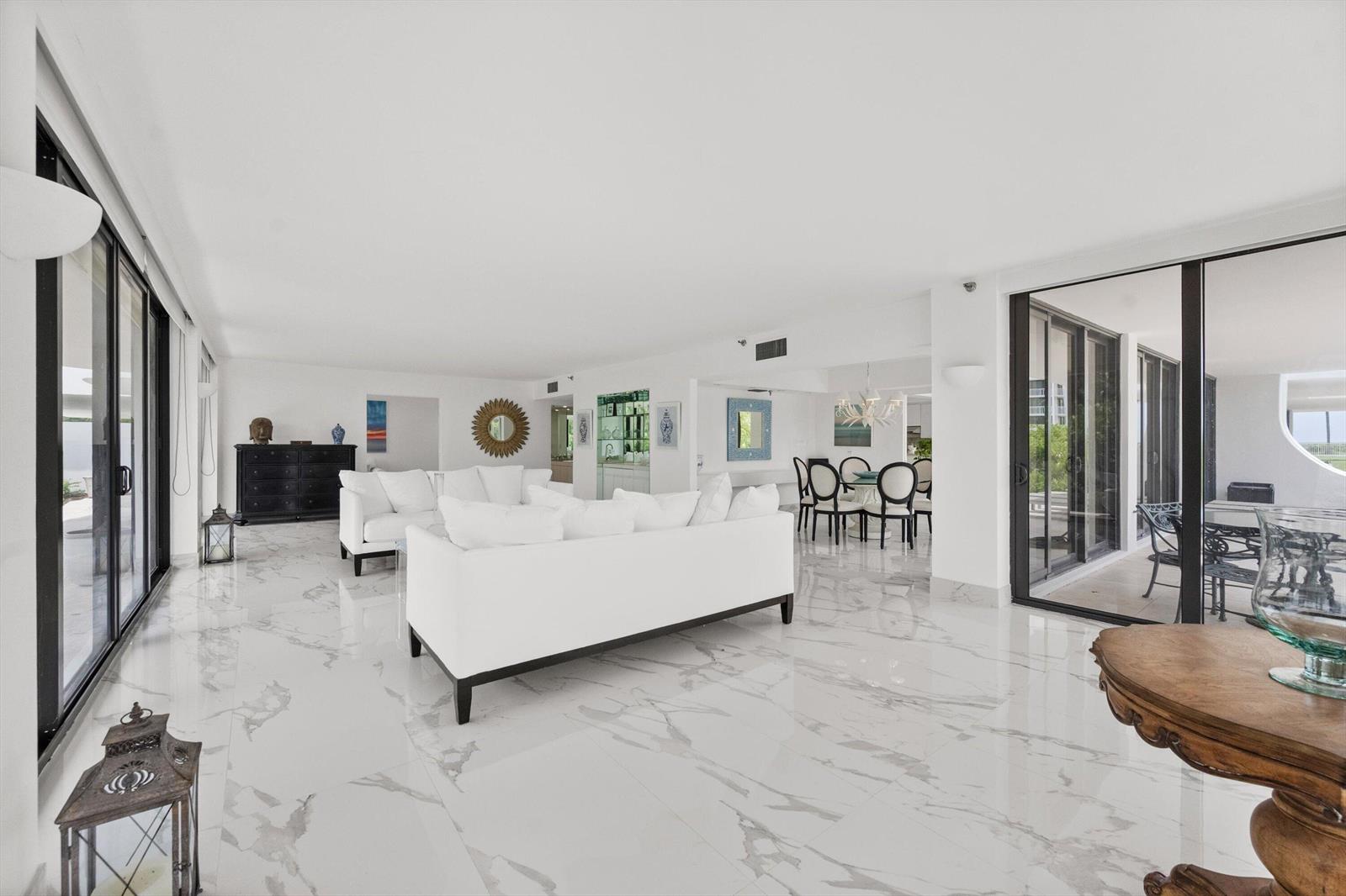 A bright living room features white marble floors, white sofas, and large glass sliding doors — 2580 S Ocean Boulevard, Palm Beach FL 33480, PALM BEACH, FL
