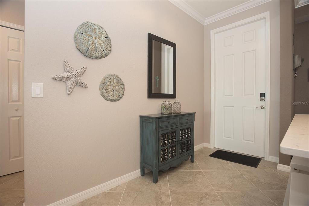 A foyer features a blue cabinet, wall-mounted coastal decor, a mirror, and a white door — 1010 TIDEWATER SHORES LOOP UNIT 204, BRADENTON, FL