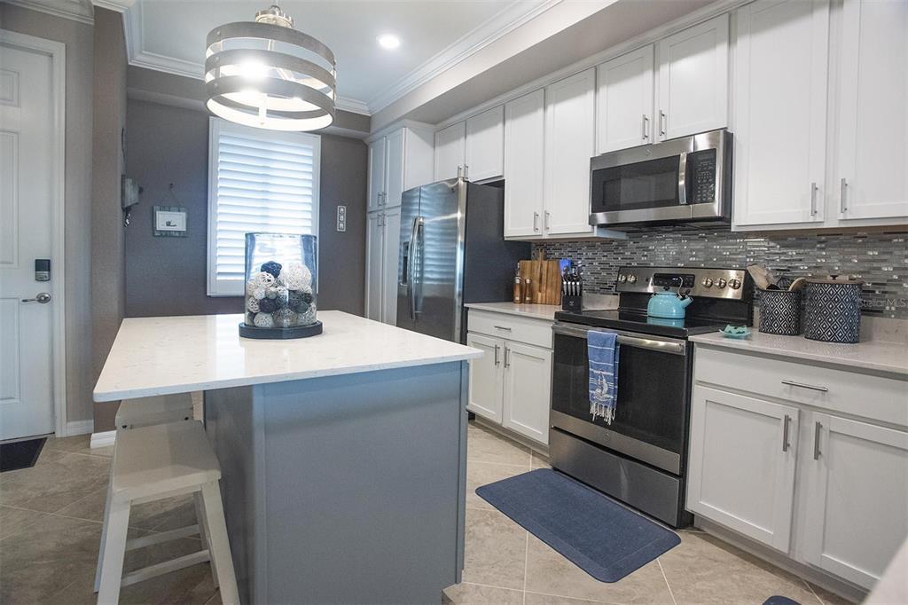 A kitchen features white cabinets, stainless steel appliances, a gray island, and a tile backsplash — 1010 TIDEWATER SHORES LOOP UNIT 204, BRADENTON, FL