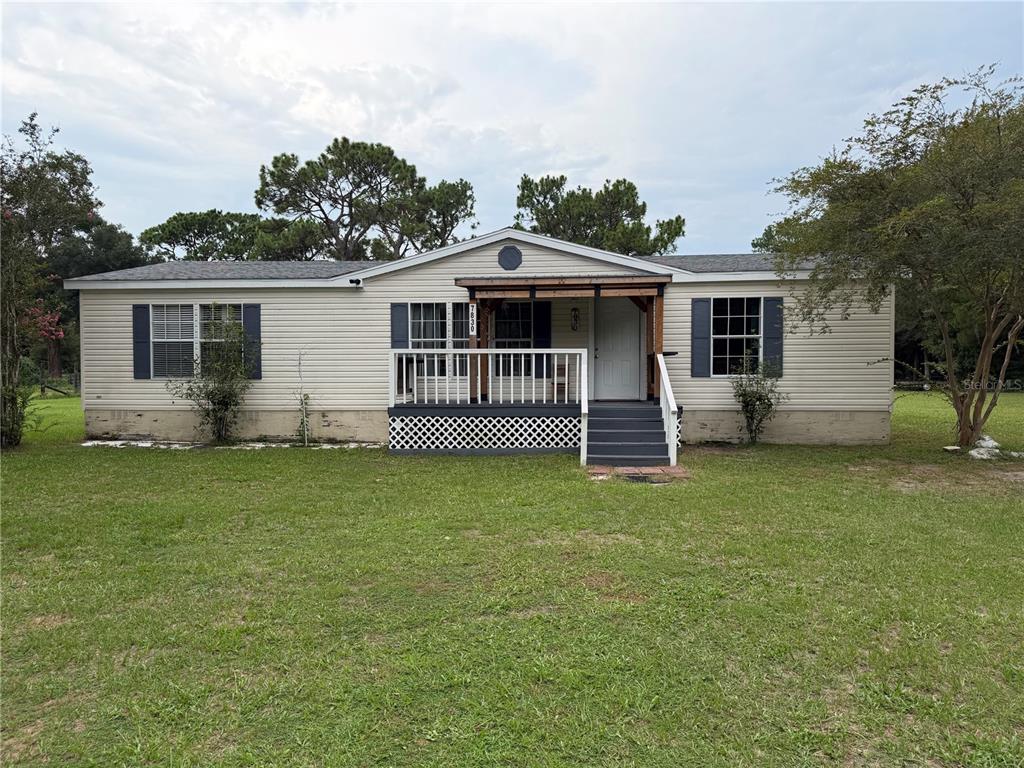 A single-story manufactured home with light siding, a front porch, and a large grassy yard — 7830 SW 19TH PLACE, OCALA, FL
