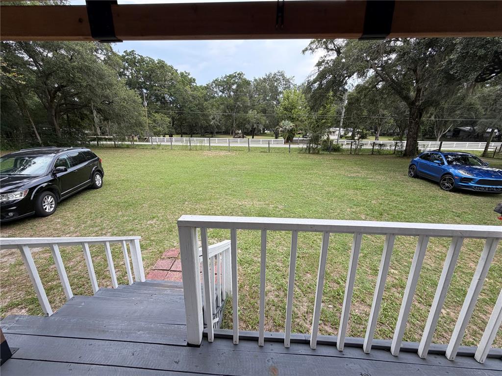 A view from a wooden deck overlooking a grassy yard with two parked cars — 7830 SW 19TH PLACE, OCALA, FL