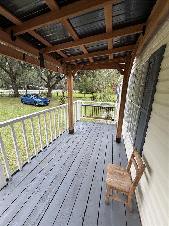 A covered wooden porch features gray decking, white railings, and a single wooden chair — 7830 SW 19TH PLACE, OCALA, FL