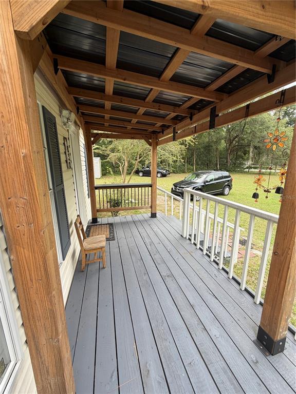 A covered wooden porch features gray decking, a single chair, and a white railing — 7830 SW 19TH PLACE, OCALA, FL
