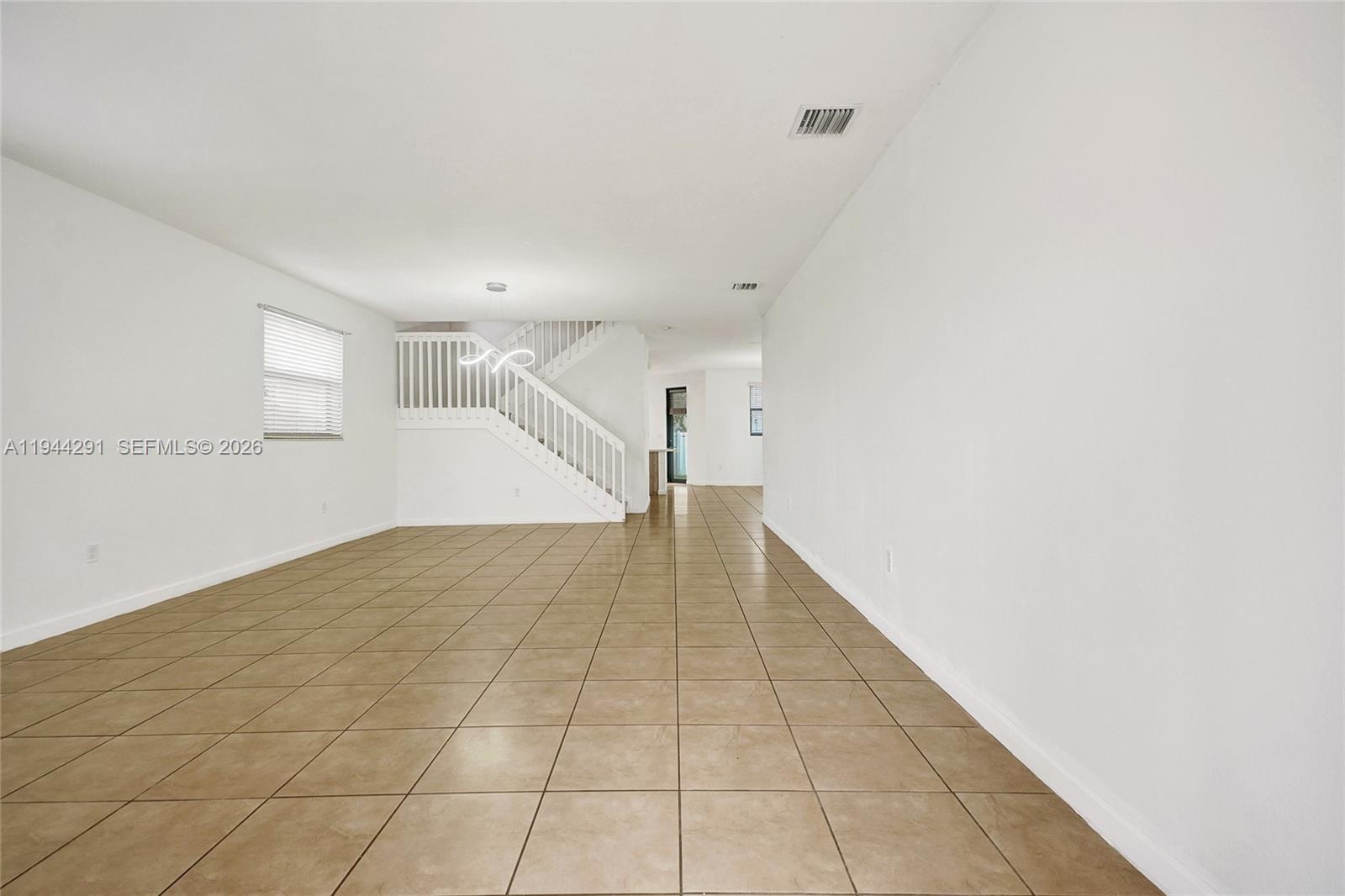 An empty room features white walls, beige tile flooring, and a white staircase — 3504 W 94th St, Hialeah FL 33018, HIALEAH, FL