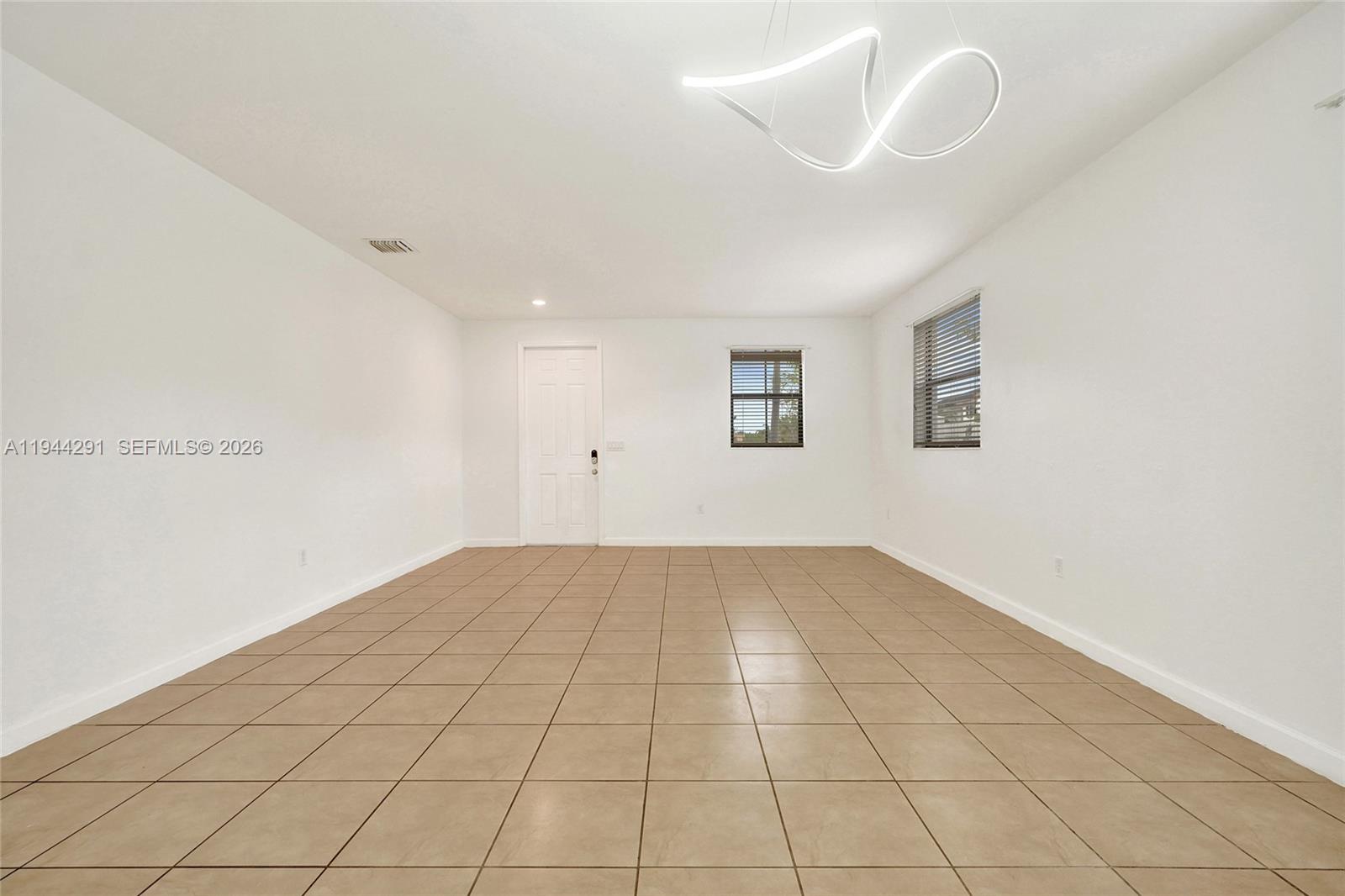 An empty room features white walls, beige tile flooring, two windows, and a modern light fixture — 3504 W 94th St, Hialeah FL 33018, HIALEAH, FL