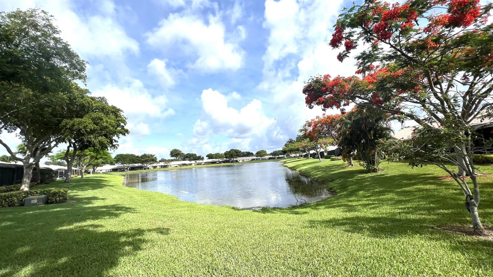 A grassy lawn slopes down to a pond surrounded by trees and residential buildings — 8743 Rheims Road # B, Boca Raton FL 33496, BOCA RATON, FL