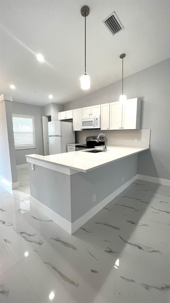 A modern kitchen features white cabinets, a quartz countertop island, and white marble-look tile flooring — 8743 Rheims Road # B, Boca Raton FL 33496, BOCA RATON, FL