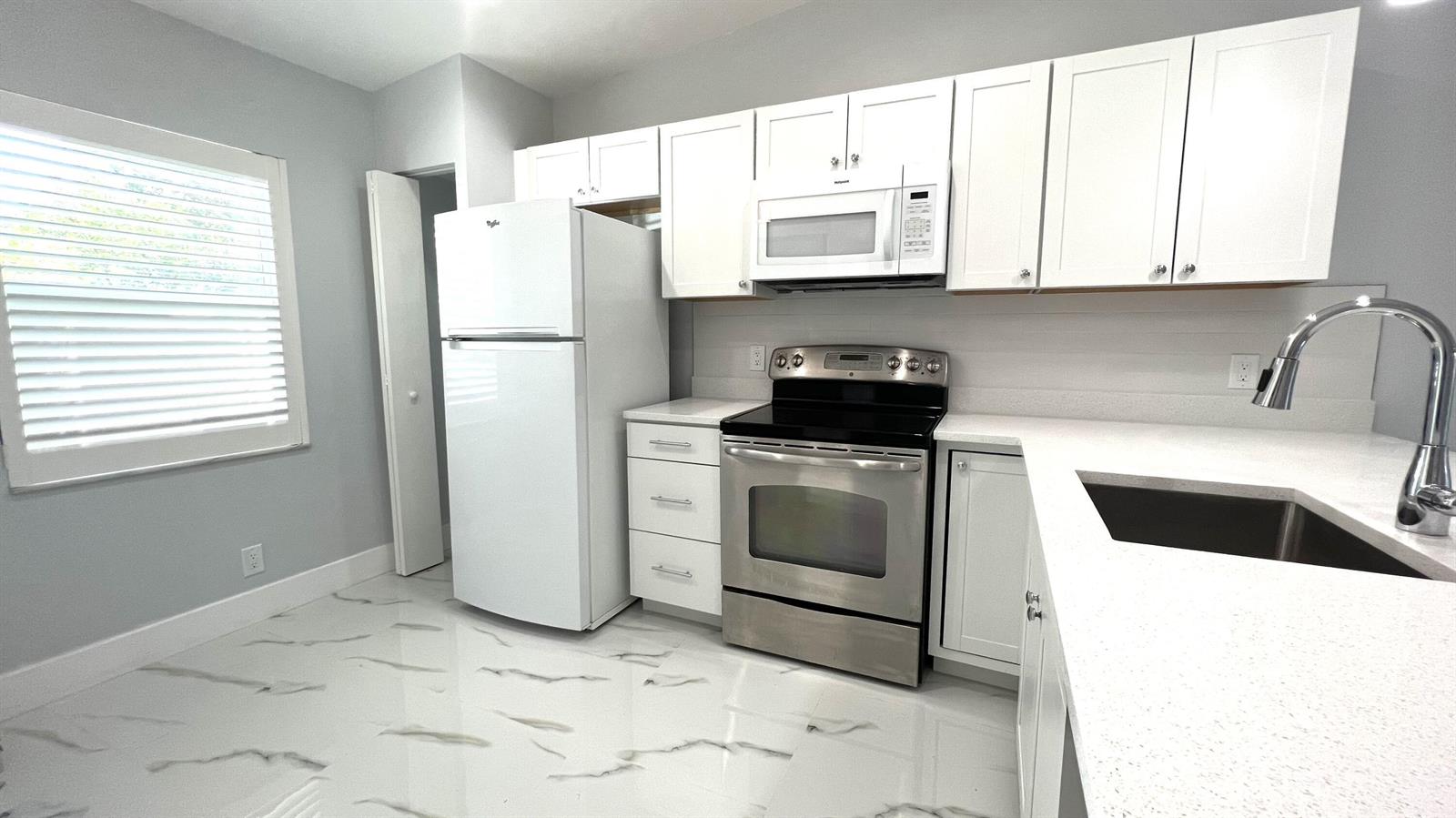 A kitchen features white cabinets, stainless steel appliances, quartz countertops, and marble-patterned tile flooring — 8743 Rheims Road # B, Boca Raton FL 33496, BOCA RATON, FL