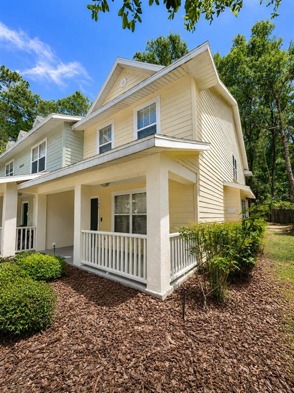 A yellow two-story townhouse features a covered front porch with white railings and landscaping — 4663 SW 48TH DRIVE UNIT 137, GAINESVILLE, FL