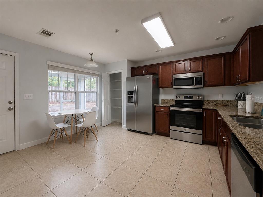 A kitchen with stainless steel appliances, dark wood cabinets, granite countertops, and a dining area — 4663 SW 48TH DRIVE UNIT 137, GAINESVILLE, FL