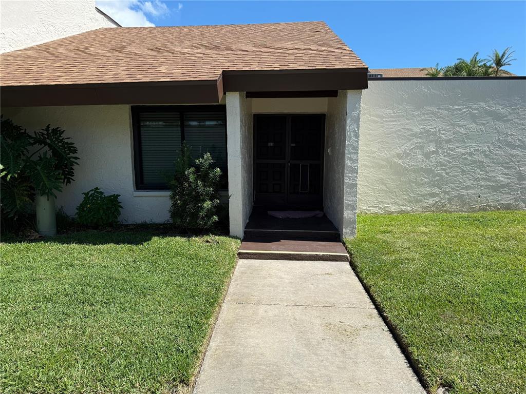 A concrete walkway leads to the front entrance of a single-story home with stucco walls — 2207 BELLEAIR ROAD UNIT B22, CLEARWATER, FL