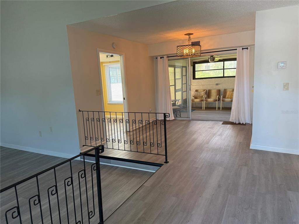 An interior view shows a living area with wood-look flooring, a metal railing, and a sunroom — 2207 BELLEAIR ROAD UNIT B22, CLEARWATER, FL