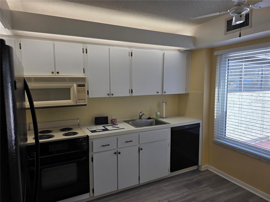 A kitchen features white cabinets, black appliances, a stainless steel sink, and light-colored flooring — 2207 BELLEAIR ROAD UNIT B22, CLEARWATER, FL