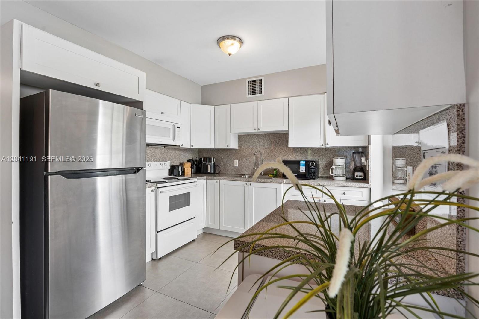 A kitchen features white cabinetry, stainless steel appliances, and granite countertops — 435 NE 69th St # 1, Miami FL 33138, MIAMI, FL