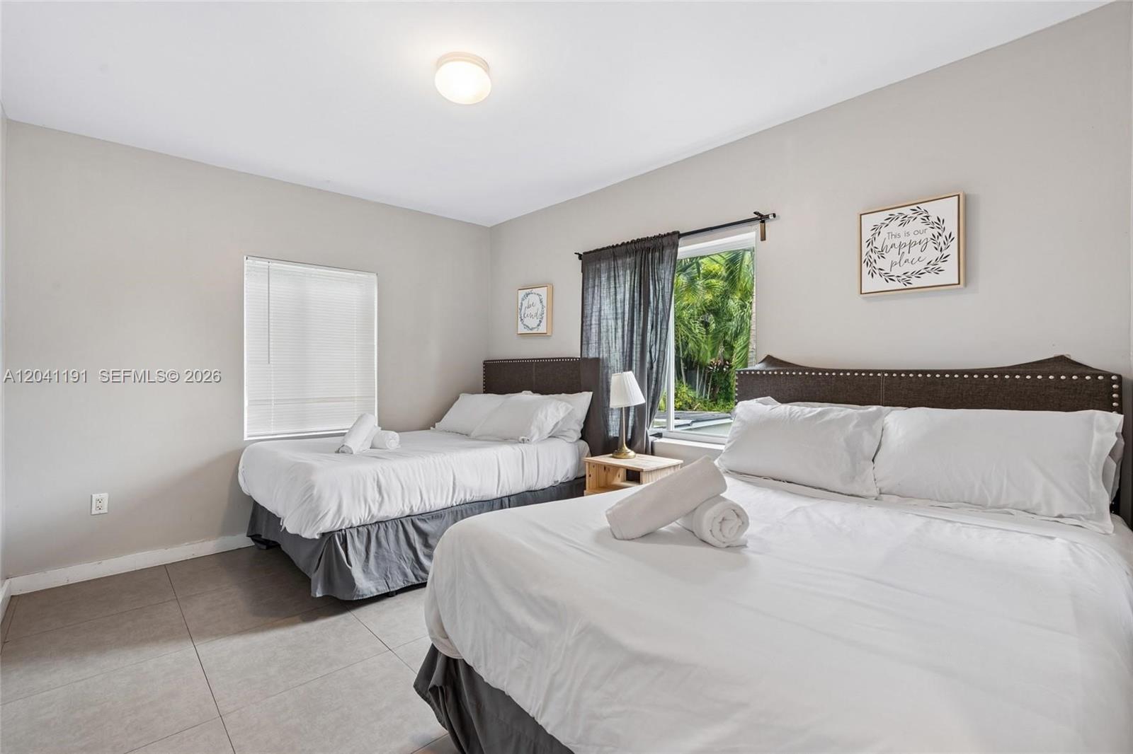 A bedroom features two beds with dark headboards, tiled floors, and a window with curtains — 435 NE 69th St # 1, Miami FL 33138, MIAMI, FL