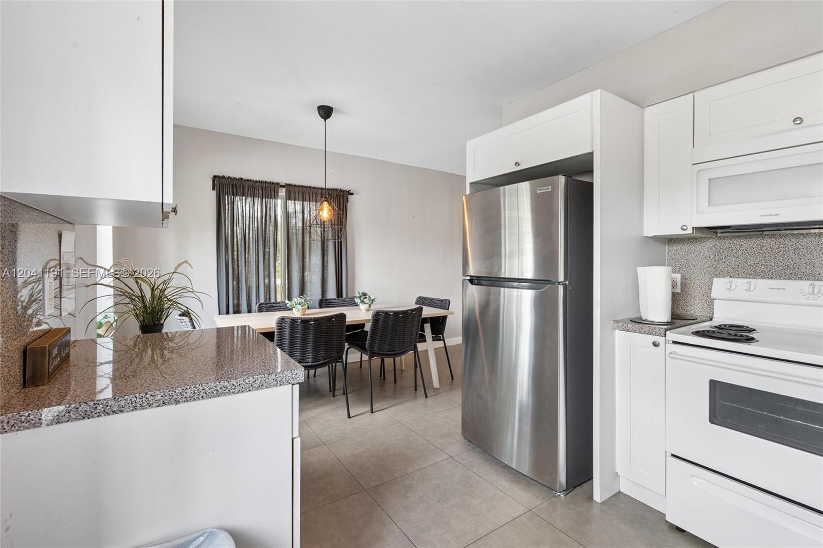 A kitchen with white cabinets, stainless steel appliances, and a dining area with dark chairs — 435 NE 69th St # 1, Miami FL 33138, MIAMI, FL