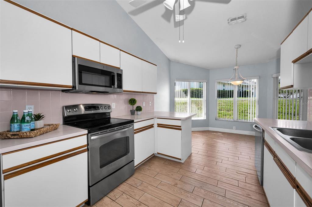 A kitchen features white cabinets, stainless steel appliances, pink tile backsplash, and wood-look tile flooring — 8919 KEATS DRIVE, HUDSON, FL