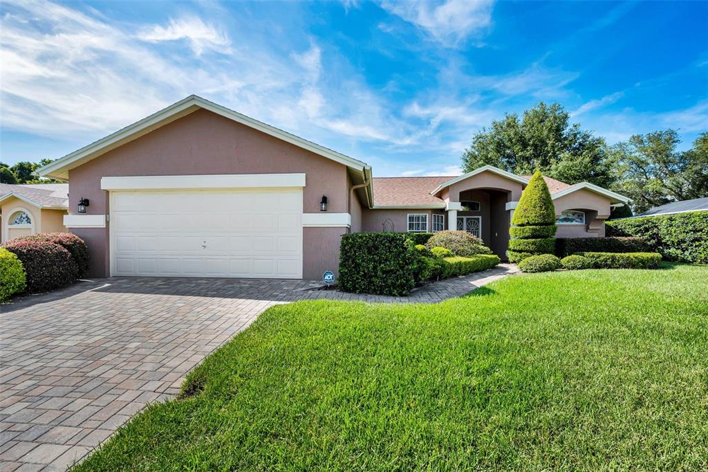 A single-story house with a two-car garage, paved driveway, and manicured landscaping under a blue sky — 8919 KEATS DRIVE, HUDSON, FL